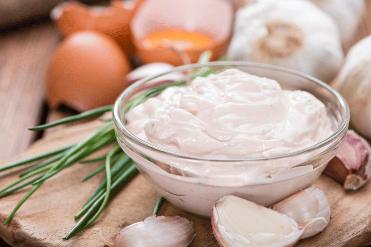 Homemade aioli in a glass small bowl on a wooden kitchen table