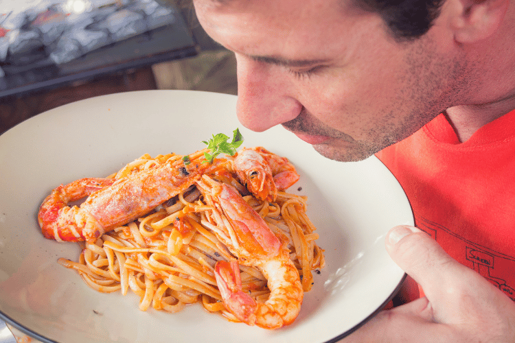 Man smelling shrimps and pasta dish on white ceramic plate