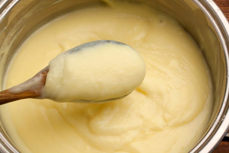 Crème pâtissière on a wooden spoon in a pot