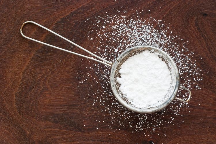 Powdered sugar in mesh strainer on a wooden background